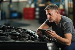 Imagem que mostra um mecânico com um tablet na frente de um motor de carro